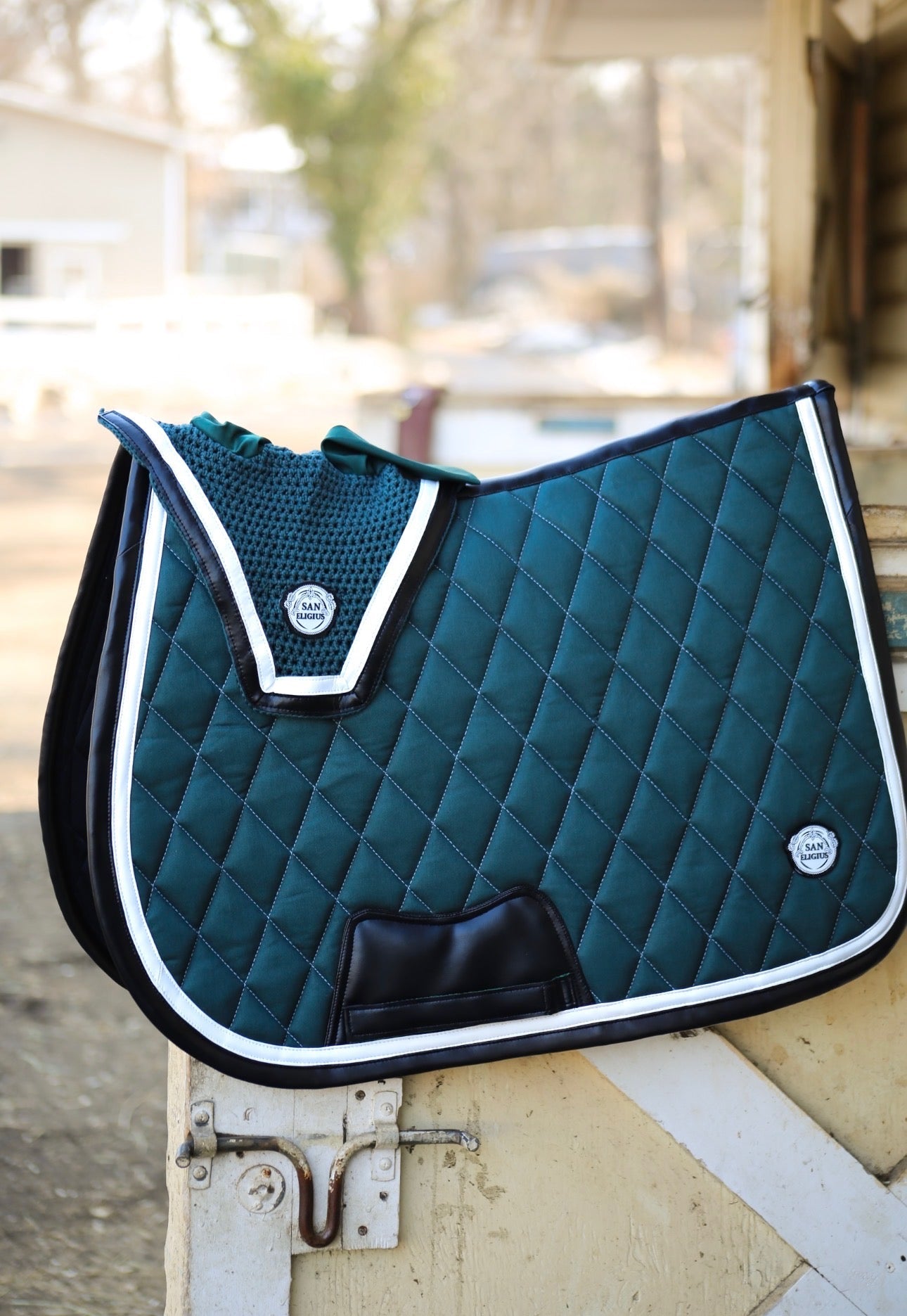 Teal quilted saddle pad with white trim on a wooden surface.