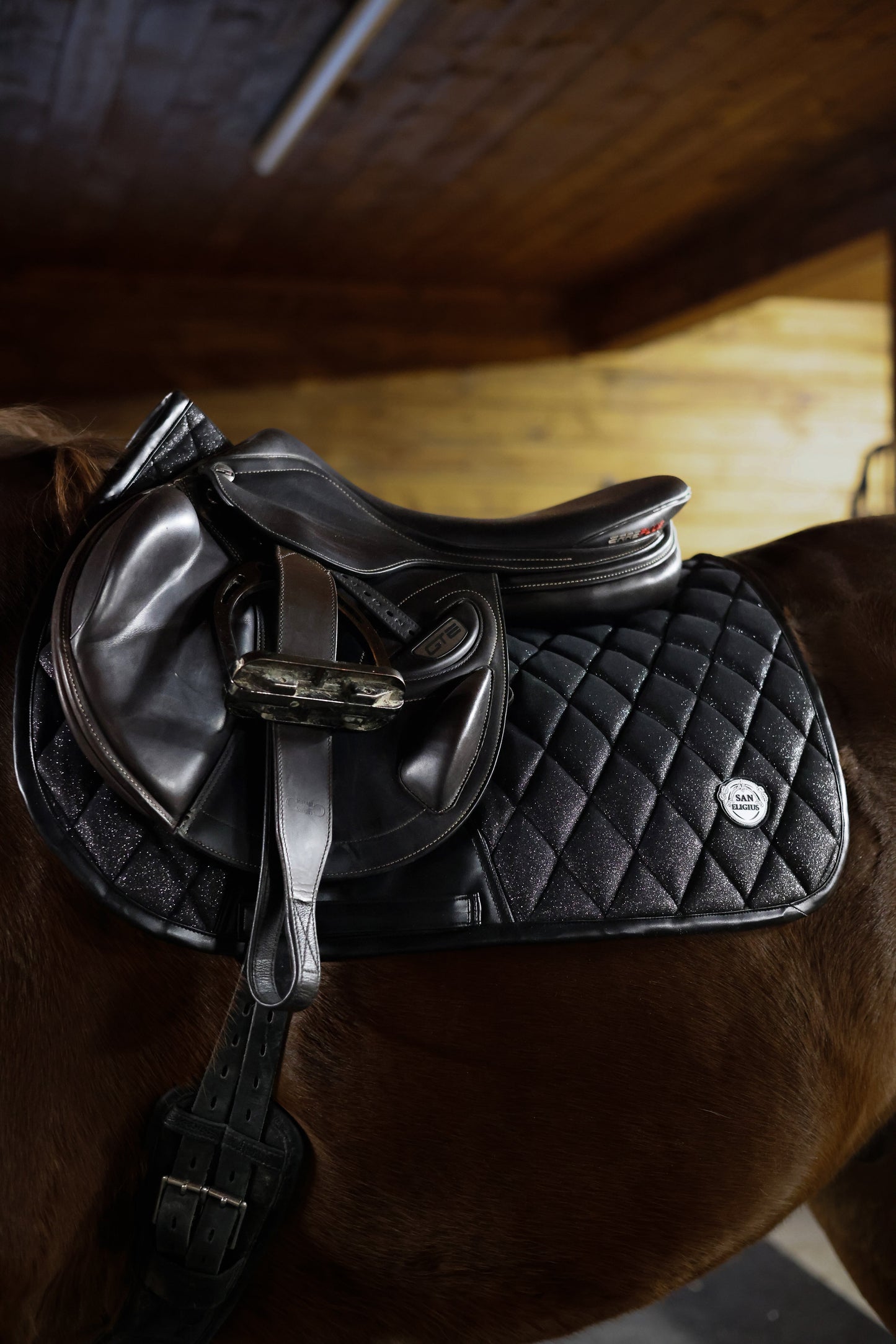 Black quilted saddle pad on a horse with a wooden floor in the background