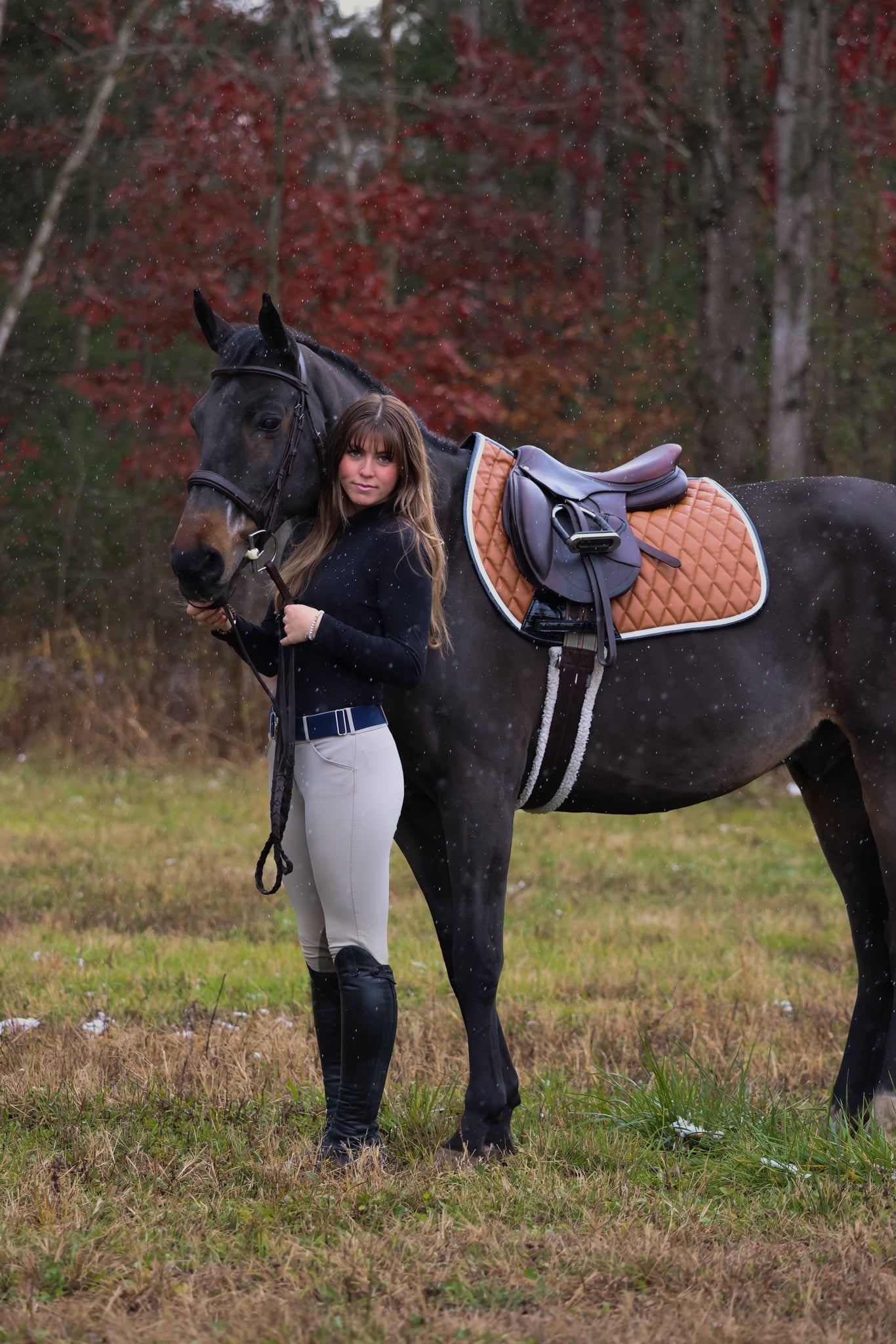 Woman standing next to a horse in a field with trees in the background