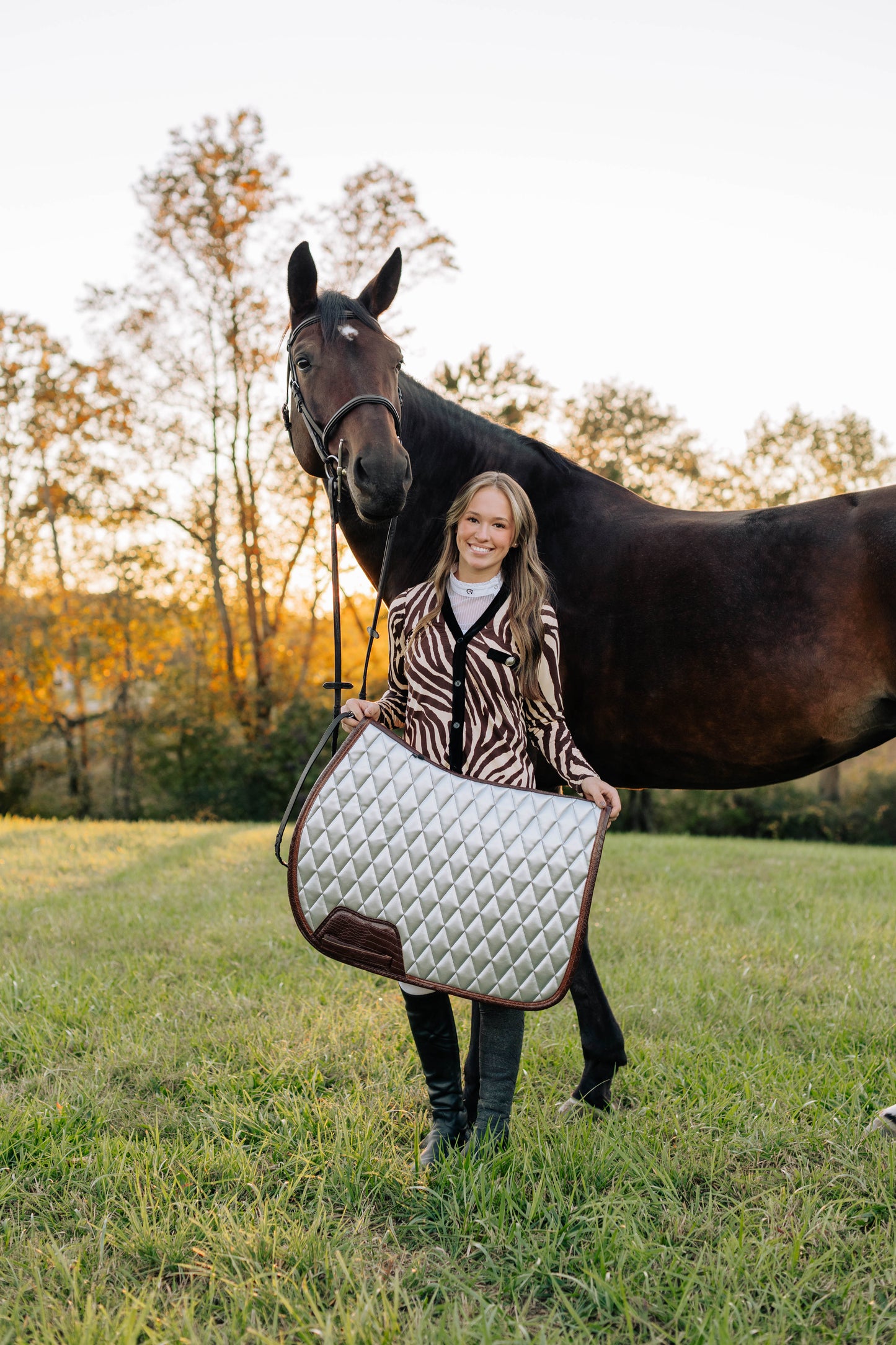 Woman holding a quilted saddle pad next to a horse in an outdoor setting