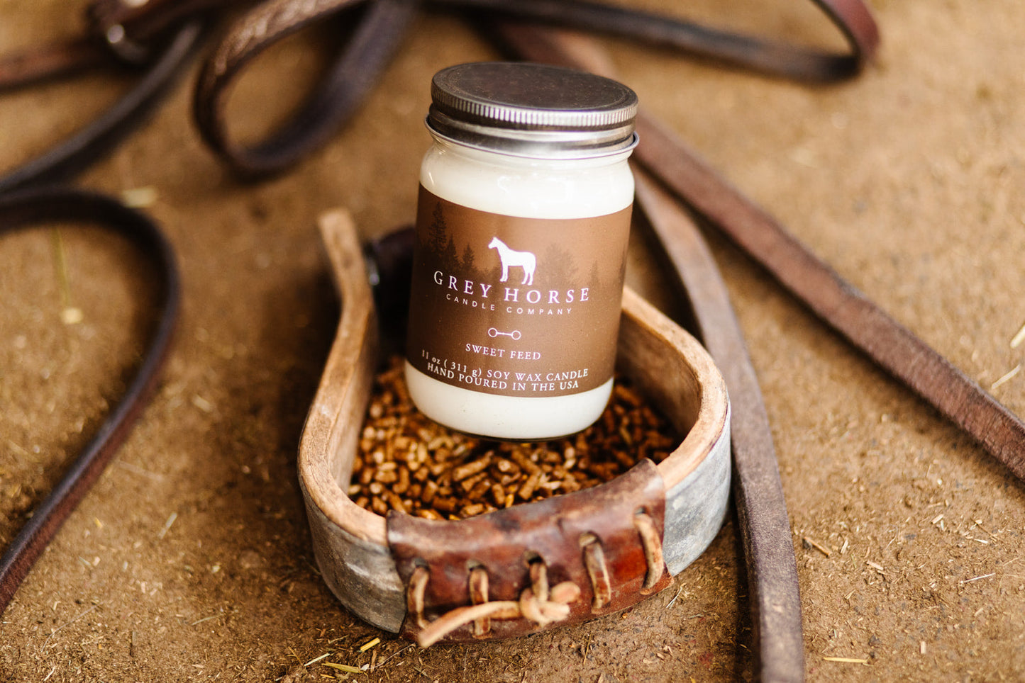 Jar of Grey Horse candle products on a rustic background with leather straps.