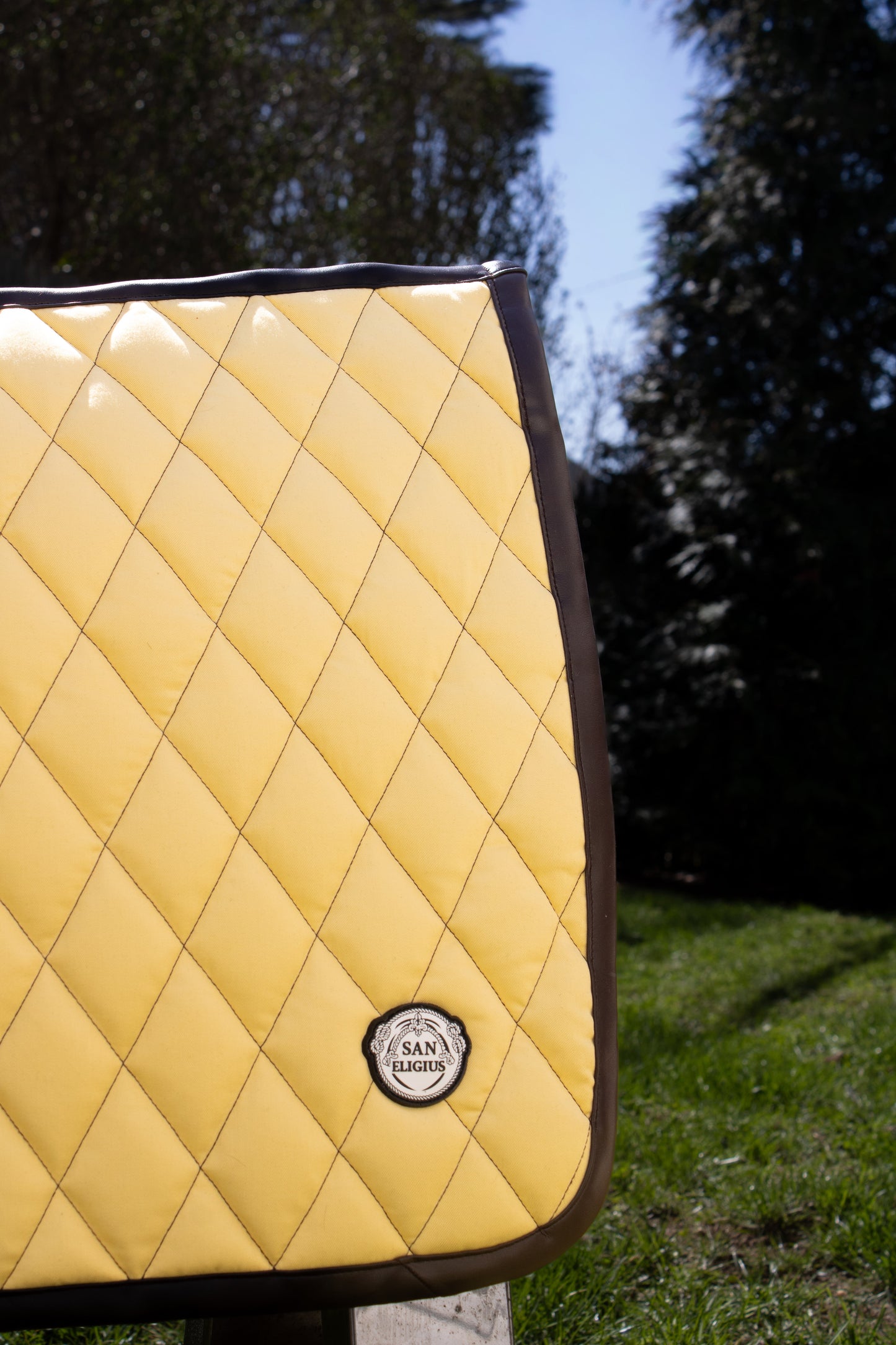 Yellow quilted saddle pad with a brand logo on a grassy background