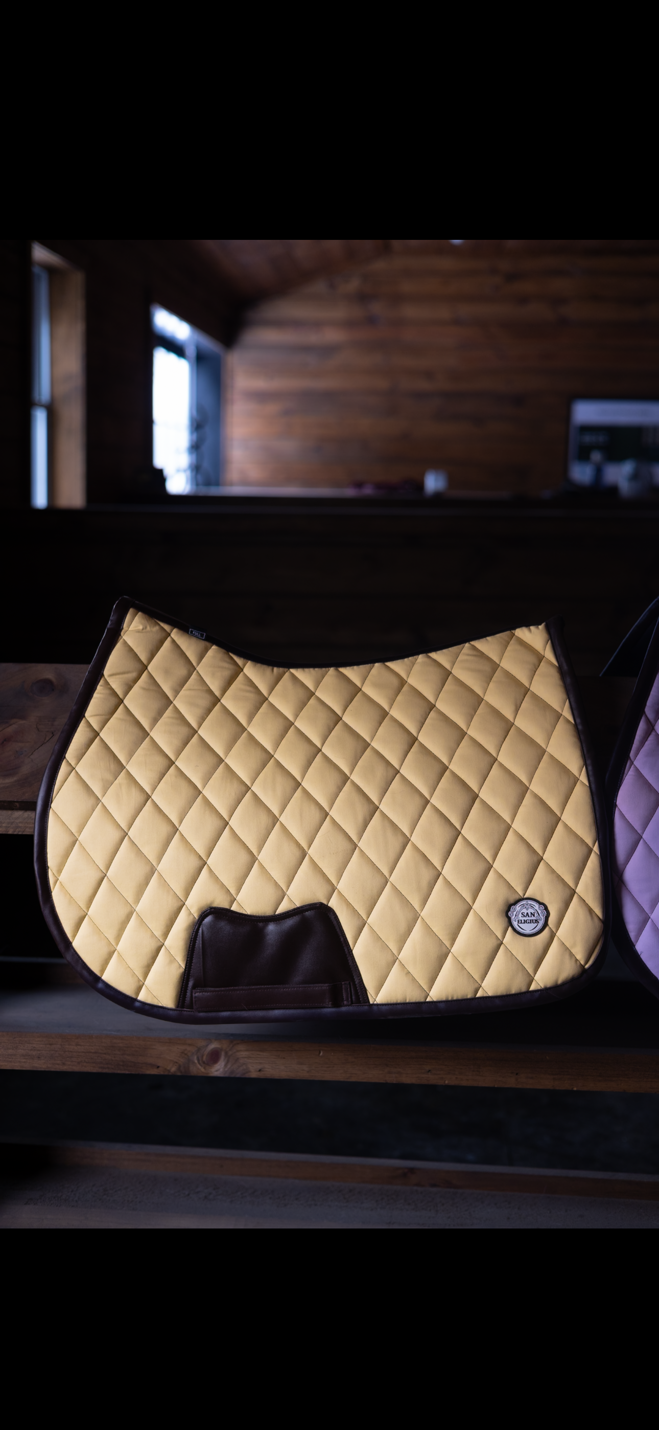 Beige quilted saddle pad on a wooden surface with a blurred background