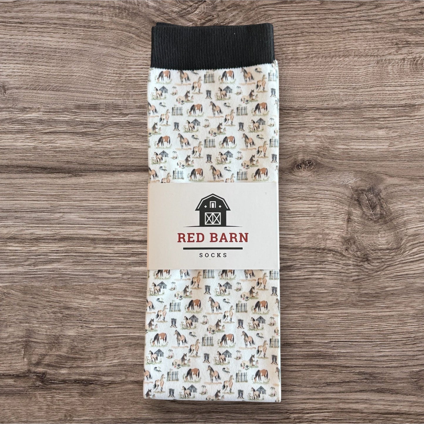 Pack of socks with horse pattern packaging on a wooden surface, featuring 'Red Barn Socks' branding.