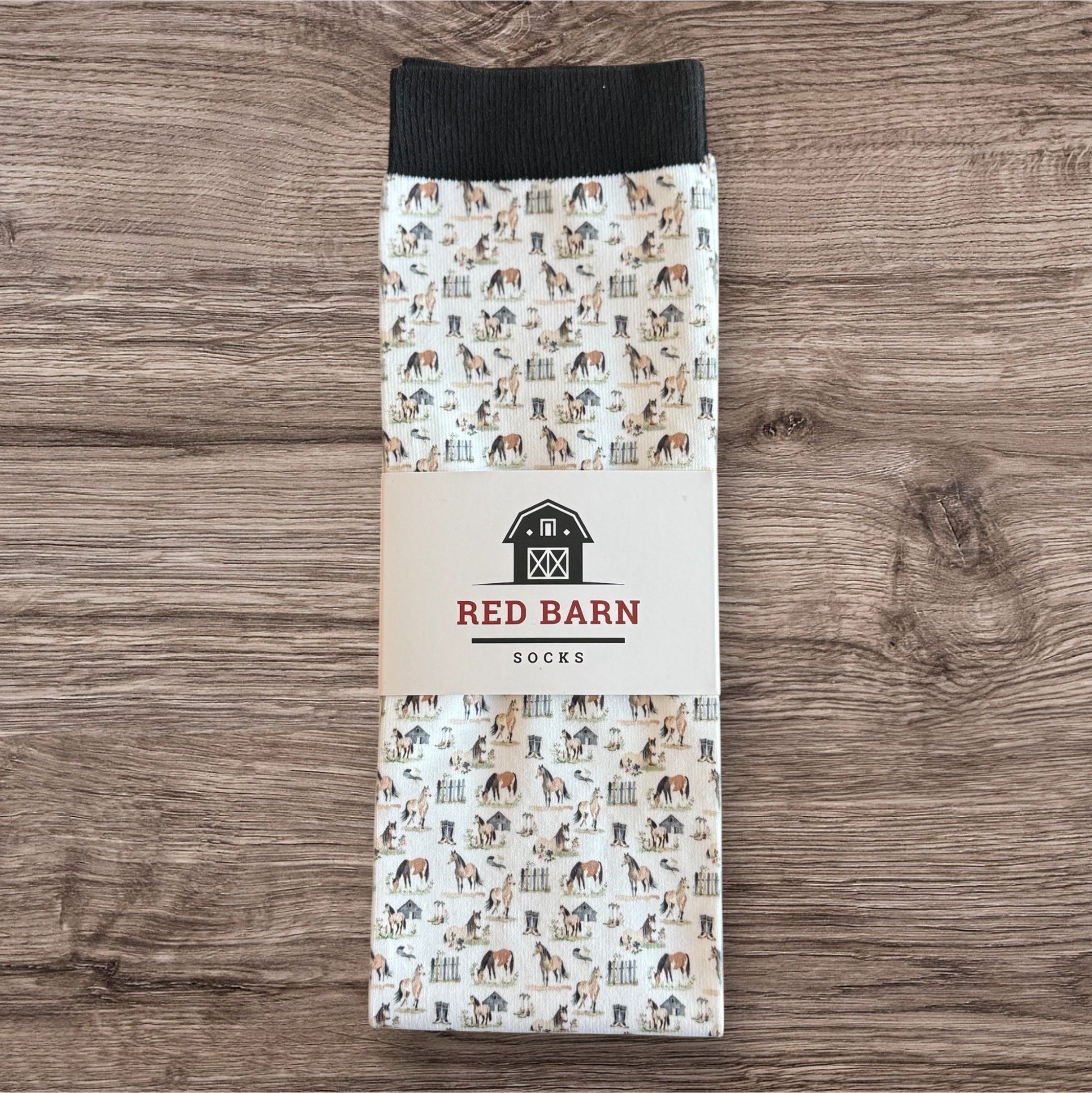 Pack of socks with horse pattern packaging on a wooden surface, featuring 'Red Barn Socks' branding.