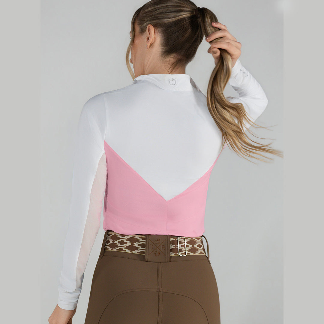 Person wearing a pink and white equestrian top with brown riding pants on a plain background
