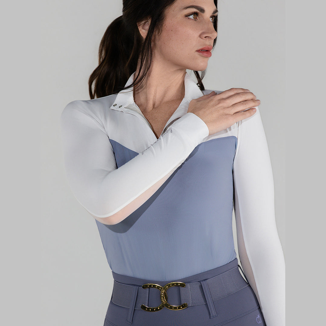 Woman wearing a two-tone equestrian outfit with a white shirt and blue vest on a gray background
