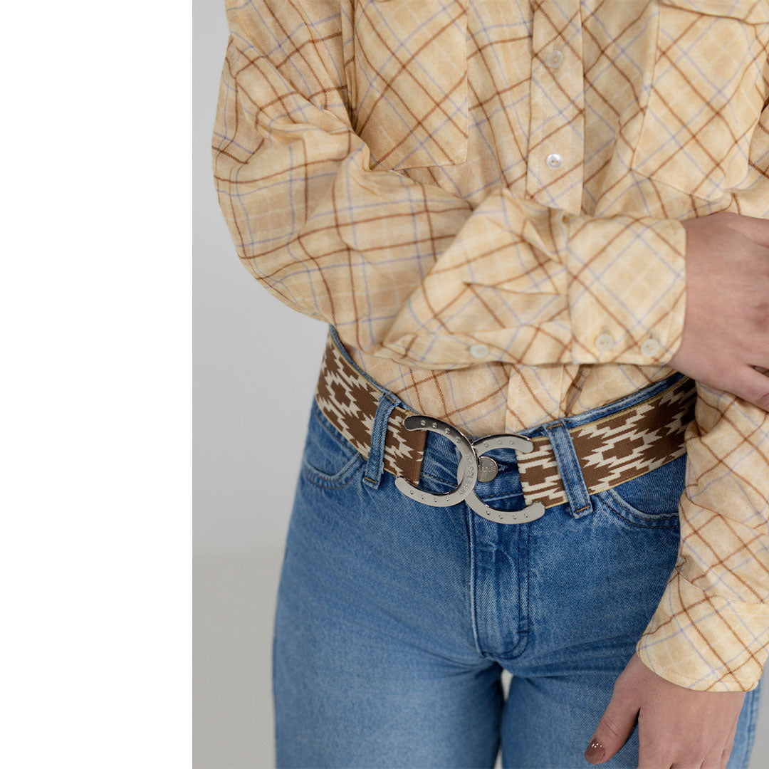 Person wearing a yellow plaid shirt and blue jeans with a patterned belt on a plain background
