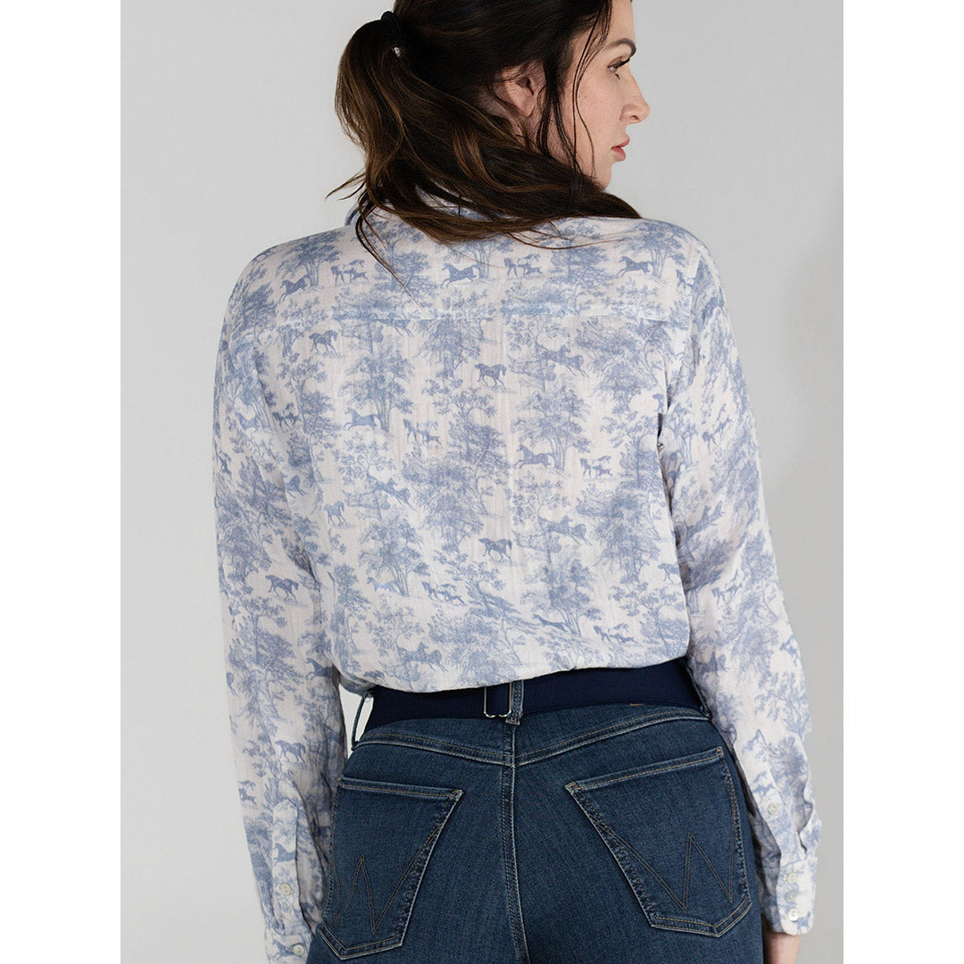 Woman wearing a light blue floral blouse and dark jeans on a gray background