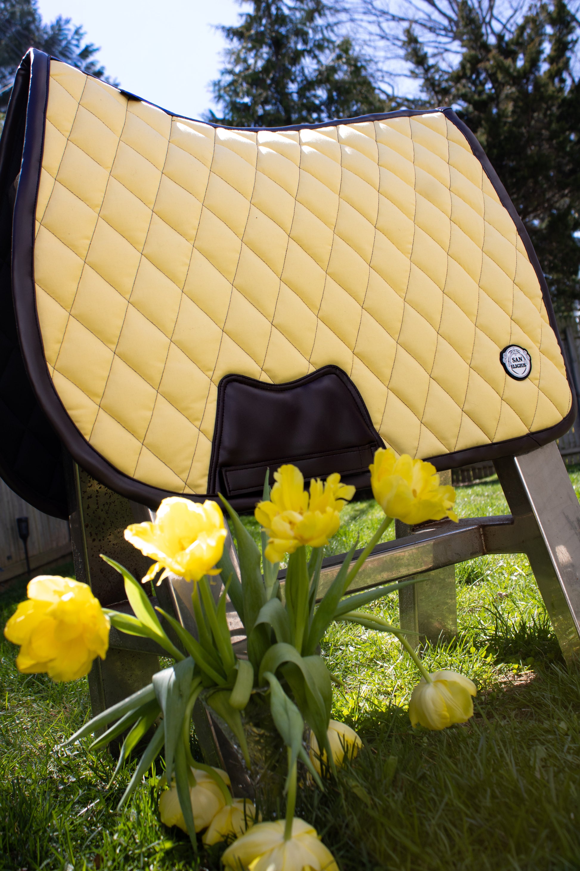 Yellow quilted saddle pad with a black border on a grassy background with yellow tulips.