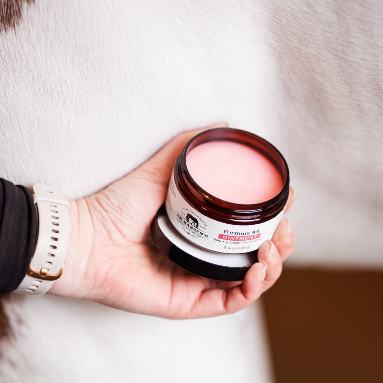 Hand holding a jar of pink cream with a white label against a blurred background
