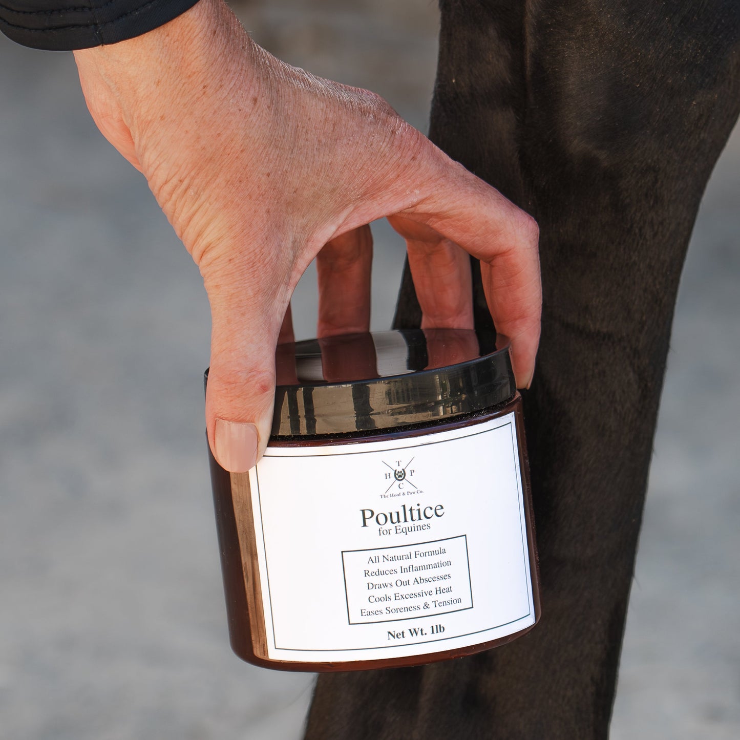 Hand holding a jar labeled 'Poultice' against a blurred background