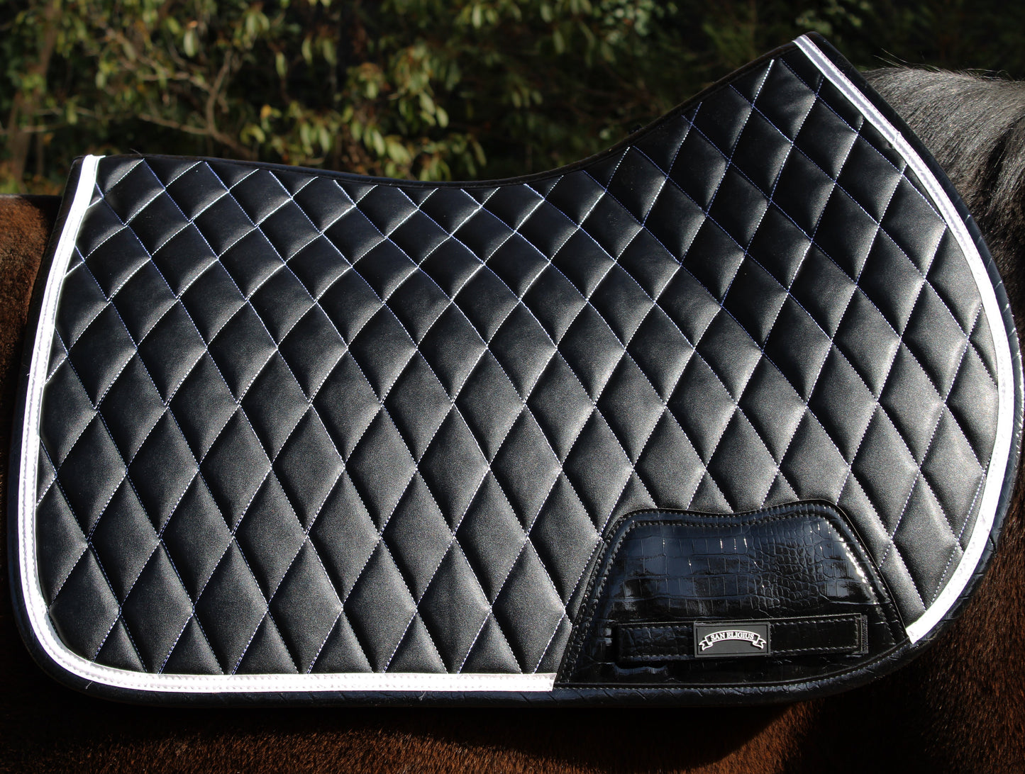 Black quilted saddle pad on a horse with a blurred natural background