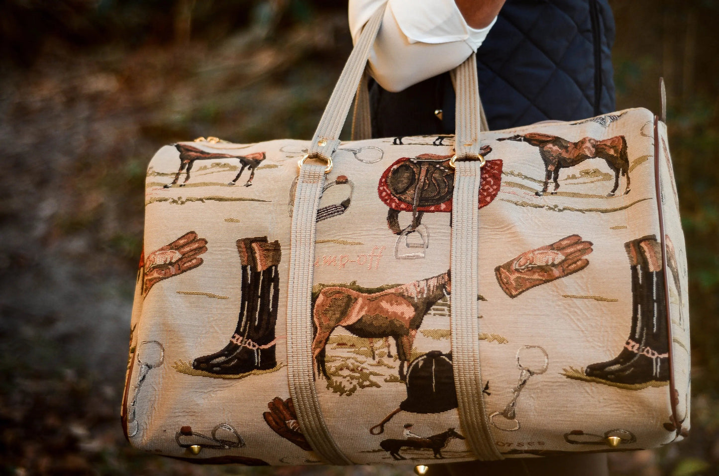 Handbag with horse and boot pattern held by a person outdoors