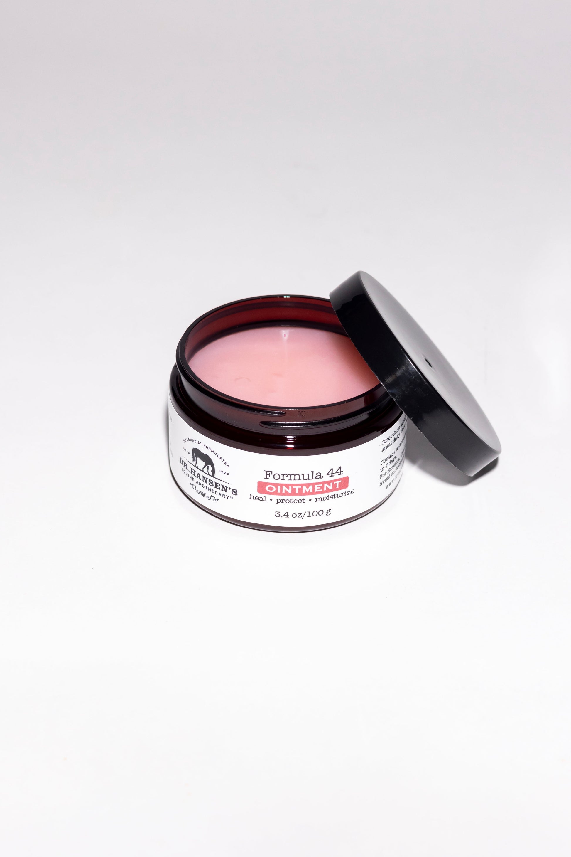 Open jar of pink ointment with visible label on a white background