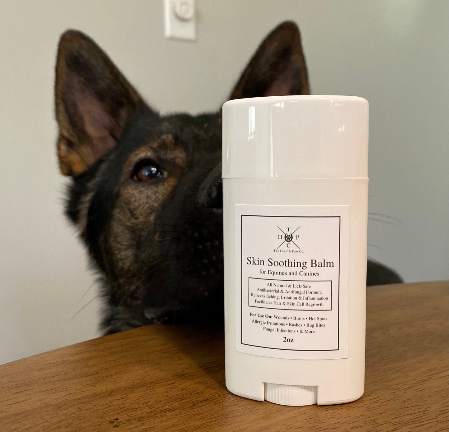 White skin soothing balm container on a wooden surface with a dog in the background